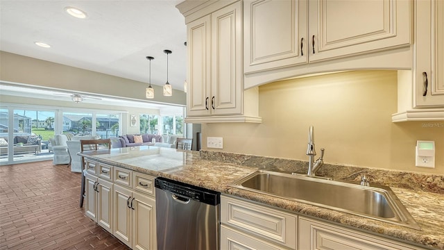 kitchen with light stone countertops, sink, stainless steel dishwasher, cream cabinets, and decorative light fixtures