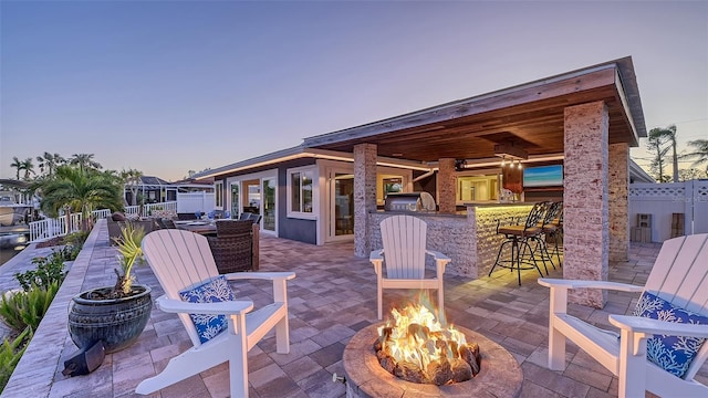 patio terrace at dusk with an outdoor kitchen, an outdoor bar, and an outdoor fire pit