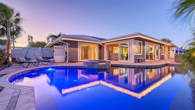 pool at dusk with an in ground hot tub and a patio