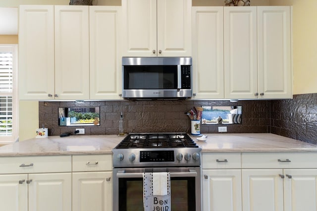 kitchen with white cabinetry, light stone counters, appliances with stainless steel finishes, and plenty of natural light