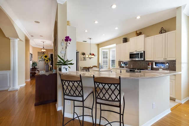 kitchen featuring ornate columns, hanging light fixtures, kitchen peninsula, a breakfast bar, and appliances with stainless steel finishes