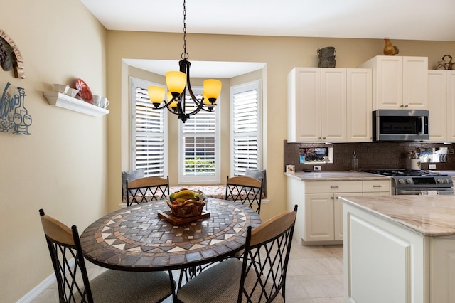 kitchen featuring decorative backsplash, white cabinets, appliances with stainless steel finishes, light stone countertops, and decorative light fixtures