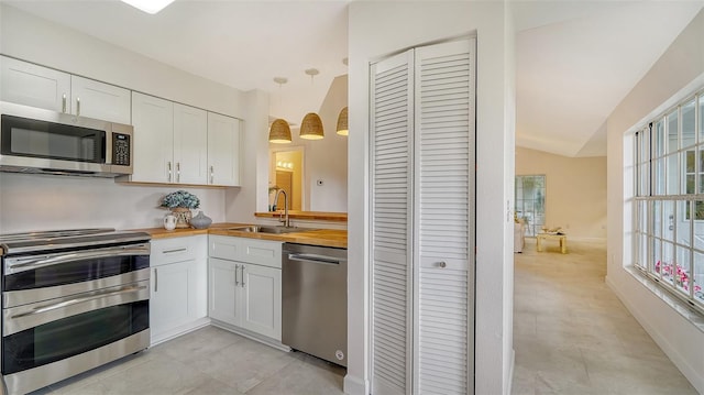 kitchen with stainless steel appliances, wooden counters, white cabinetry, a sink, and baseboards