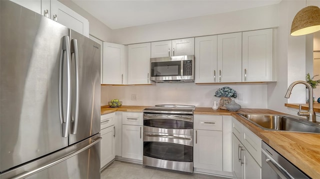 kitchen with a sink, white cabinetry, stainless steel appliances, and wooden counters