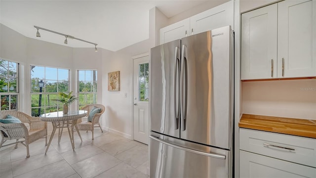 kitchen featuring baseboards, light tile patterned flooring, freestanding refrigerator, and white cabinets