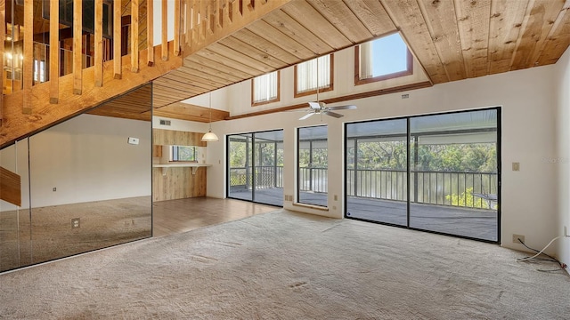 unfurnished living room with ceiling fan, wooden ceiling, carpet flooring, a skylight, and a high ceiling