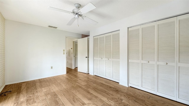 unfurnished bedroom with ceiling fan, a textured ceiling, light hardwood / wood-style flooring, and two closets