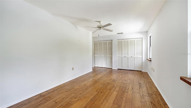 unfurnished bedroom featuring two closets, a textured ceiling, light hardwood / wood-style floors, and ceiling fan