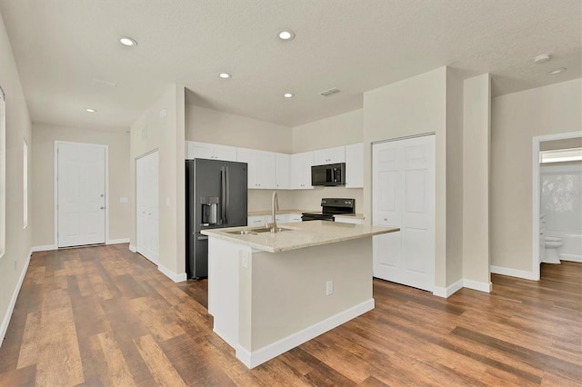 kitchen featuring black appliances, an island with sink, wood-type flooring, and white cabinetry