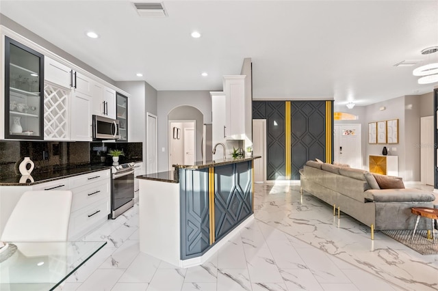 kitchen featuring kitchen peninsula, decorative backsplash, white cabinets, and appliances with stainless steel finishes