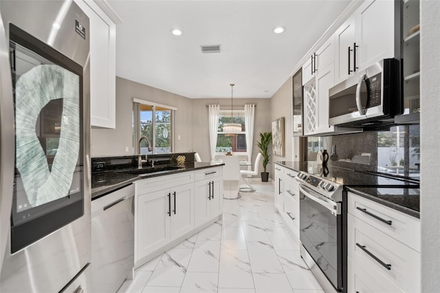 kitchen with appliances with stainless steel finishes, sink, dark stone countertops, white cabinets, and hanging light fixtures