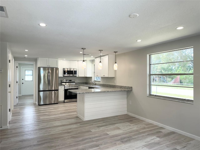 kitchen featuring kitchen peninsula, pendant lighting, white cabinetry, appliances with stainless steel finishes, and light hardwood / wood-style floors