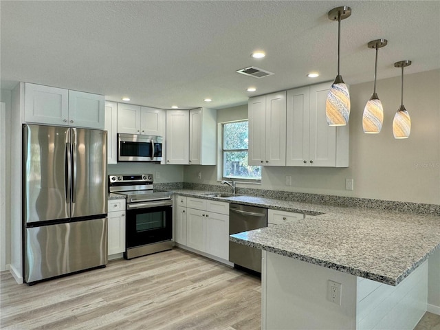 kitchen featuring appliances with stainless steel finishes, decorative light fixtures, kitchen peninsula, and white cabinets