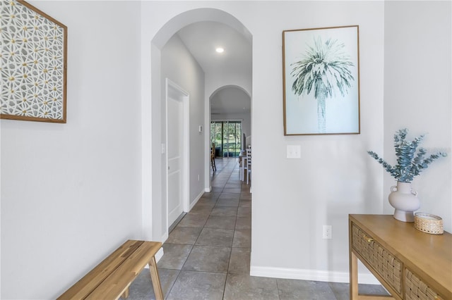 corridor featuring arched walkways, tile patterned floors, and baseboards