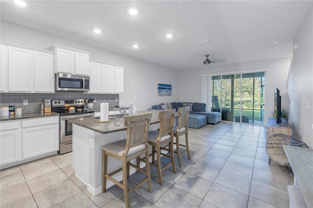 kitchen with dark stone countertops, stainless steel appliances, white cabinetry, and an island with sink