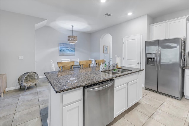 kitchen with stainless steel appliances, dark stone countertops, a center island with sink, sink, and white cabinetry