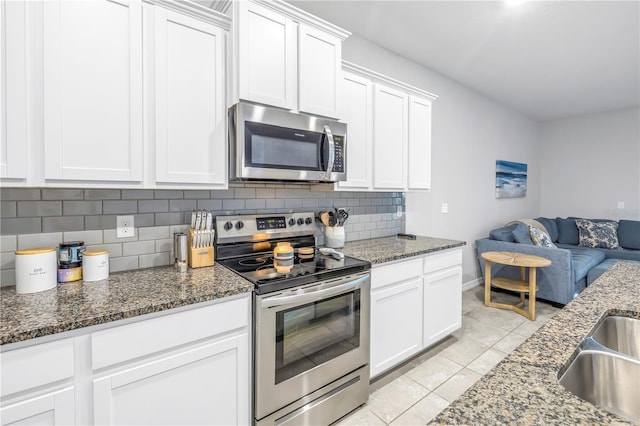 kitchen featuring white cabinets, appliances with stainless steel finishes, open floor plan, dark stone countertops, and backsplash