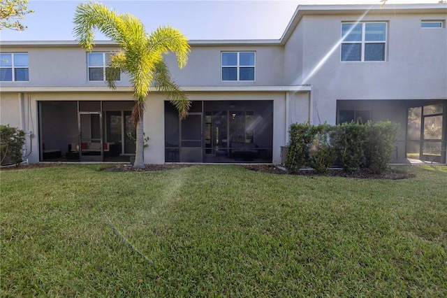 back of property featuring a sunroom, a yard, and stucco siding