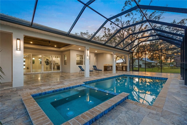 pool at dusk featuring exterior kitchen, an in ground hot tub, a lanai, and a patio area