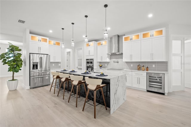 kitchen with wine cooler, wall chimney exhaust hood, white cabinets, an island with sink, and stainless steel appliances