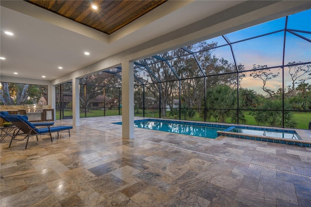 pool at dusk featuring glass enclosure, an in ground hot tub, a patio, and area for grilling