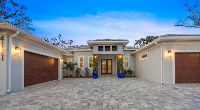 exterior entry at dusk featuring a garage and french doors