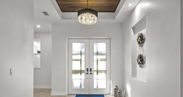 doorway featuring light wood-type flooring, a chandelier, french doors, and a raised ceiling