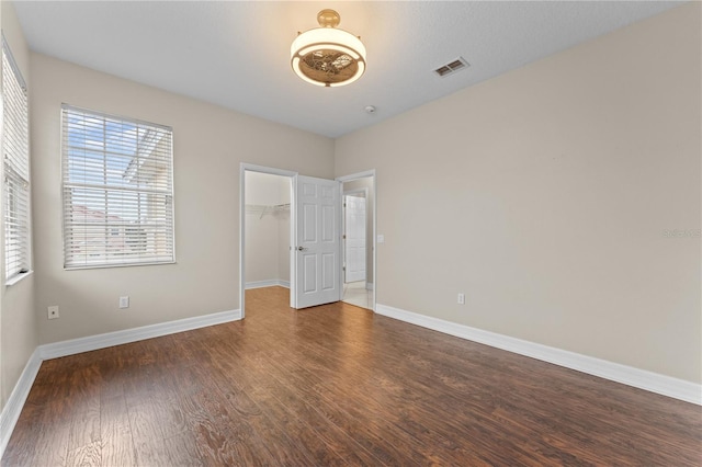 unfurnished bedroom with dark wood-type flooring, a closet, and a walk in closet