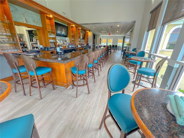 bar with dark stone countertops, light wood-type flooring, and a healthy amount of sunlight