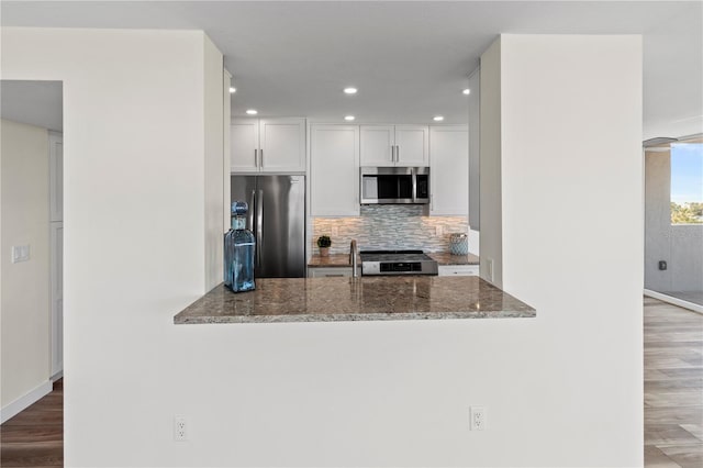 kitchen featuring kitchen peninsula, appliances with stainless steel finishes, tasteful backsplash, dark stone counters, and white cabinets