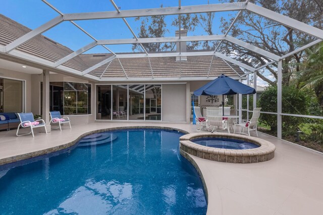 view of pool featuring glass enclosure, an in ground hot tub, and a patio area