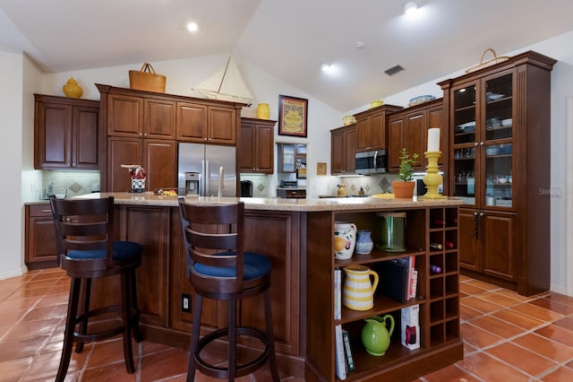 kitchen featuring stainless steel appliances, tasteful backsplash, an island with sink, lofted ceiling, and dark brown cabinets