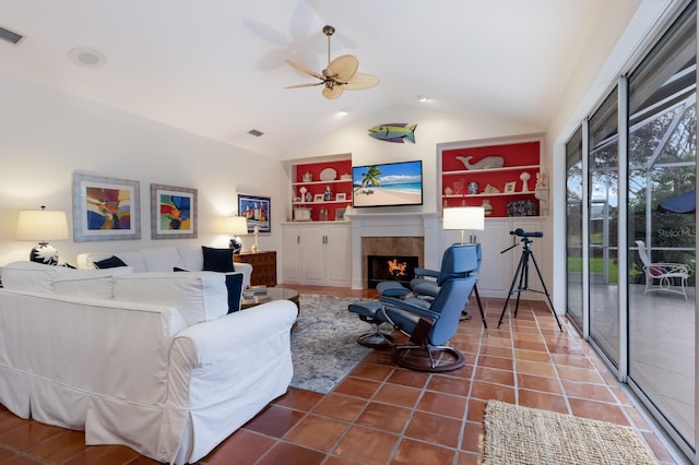 tiled living room with visible vents, built in shelves, a tiled fireplace, a ceiling fan, and vaulted ceiling