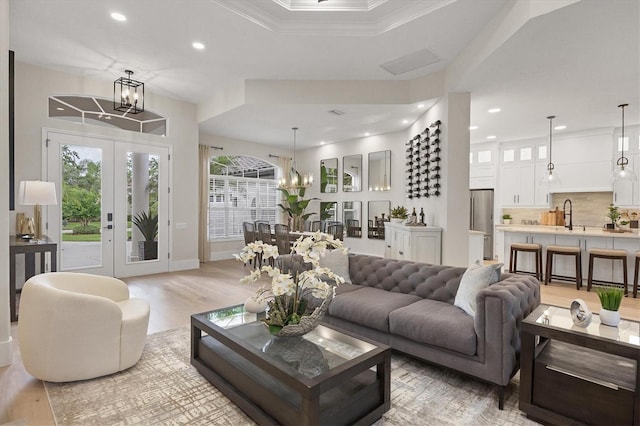 living room with an inviting chandelier, light hardwood / wood-style flooring, crown molding, french doors, and sink