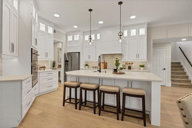 kitchen with white cabinetry, backsplash, light hardwood / wood-style flooring, and a kitchen island with sink