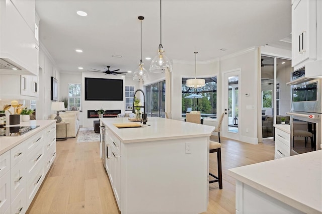 kitchen with light wood-type flooring, stainless steel double oven, white cabinetry, pendant lighting, and a center island with sink