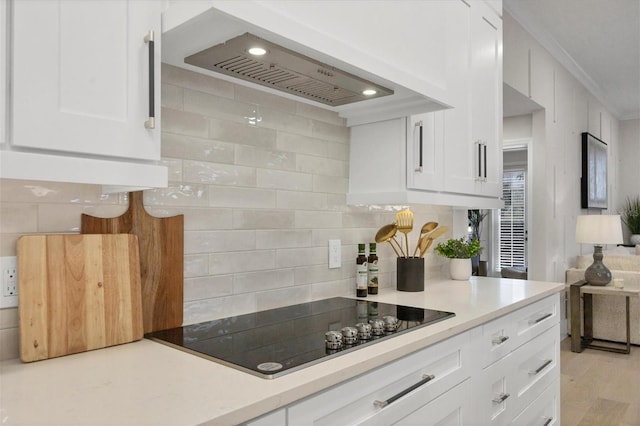 kitchen featuring black electric stovetop, wall chimney exhaust hood, ornamental molding, white cabinetry, and tasteful backsplash