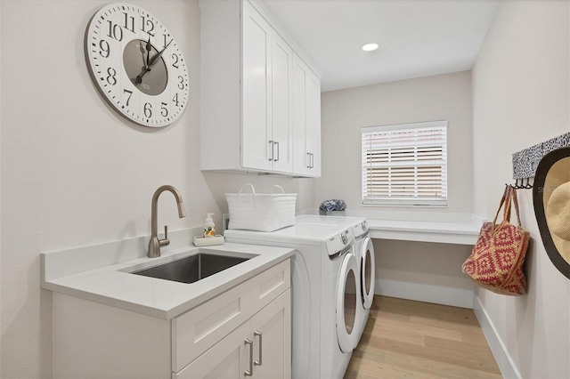 clothes washing area featuring cabinets, sink, washing machine and clothes dryer, and light wood-type flooring