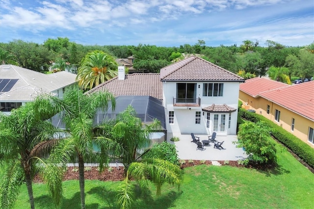 back of property with a balcony, glass enclosure, a patio, and a lawn