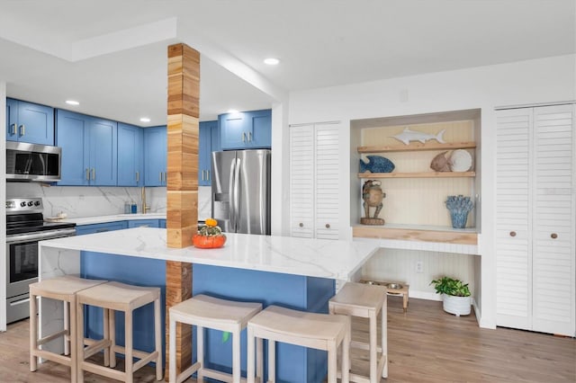 kitchen with blue cabinetry, stainless steel appliances, light wood-type flooring, and a breakfast bar area