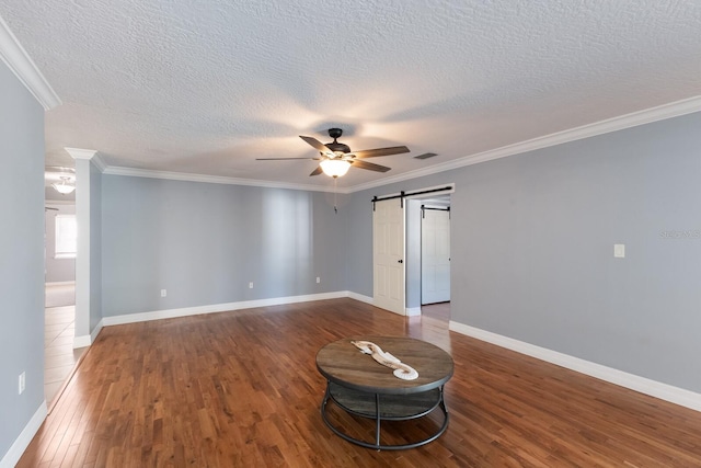 unfurnished room featuring hardwood / wood-style floors, ceiling fan, a textured ceiling, a barn door, and crown molding