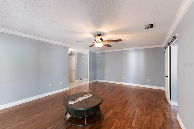 spare room featuring ceiling fan, a textured ceiling, a barn door, hardwood / wood-style flooring, and crown molding