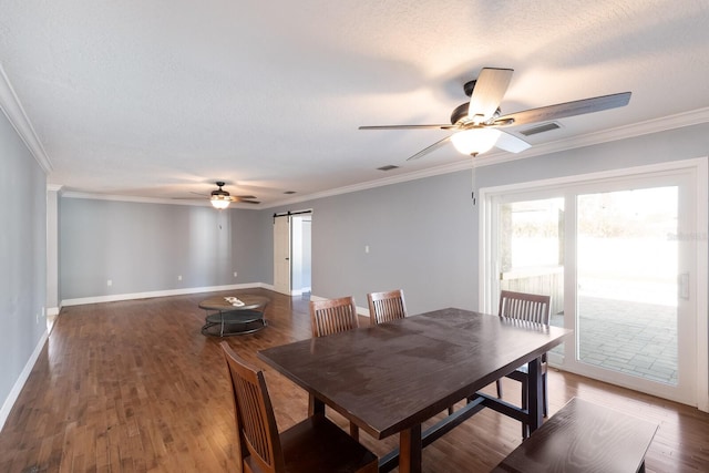 dining space with a barn door, a textured ceiling, ceiling fan, dark wood-type flooring, and crown molding