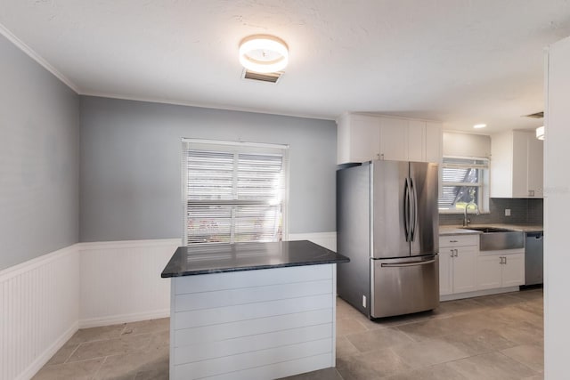 kitchen with appliances with stainless steel finishes, white cabinetry, a healthy amount of sunlight, and a kitchen island