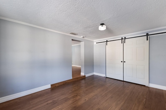 unfurnished bedroom featuring dark hardwood / wood-style floors, ornamental molding, a textured ceiling, and a barn door