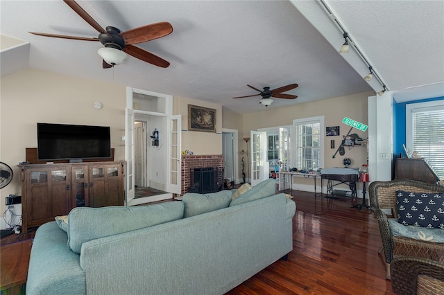 living room with a brick fireplace, a textured ceiling, a healthy amount of sunlight, and dark hardwood / wood-style flooring