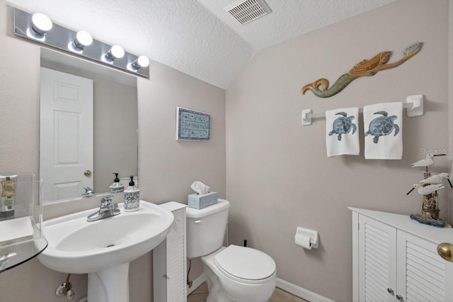 bathroom with toilet, lofted ceiling, a textured ceiling, and sink