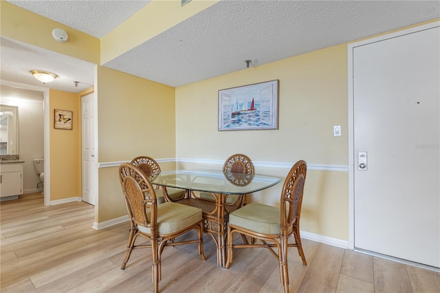 dining space with a textured ceiling and light hardwood / wood-style flooring