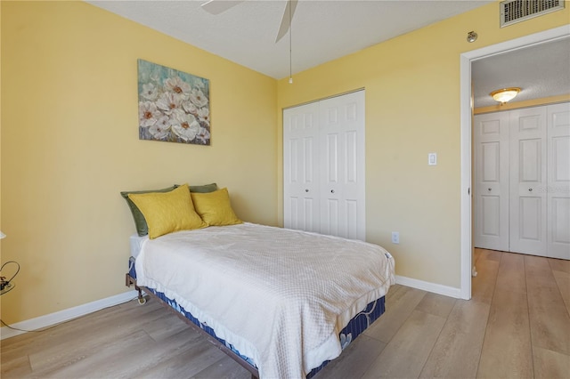 bedroom with ceiling fan, light wood-type flooring, a textured ceiling, and multiple closets