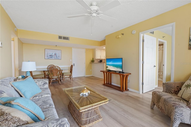 living area with a textured ceiling, ceiling fan, visible vents, baseboards, and light wood-style floors